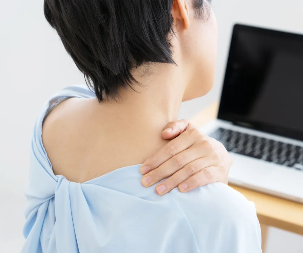 デスクワーク中に肩の疲れを気にする女性のイメージ
